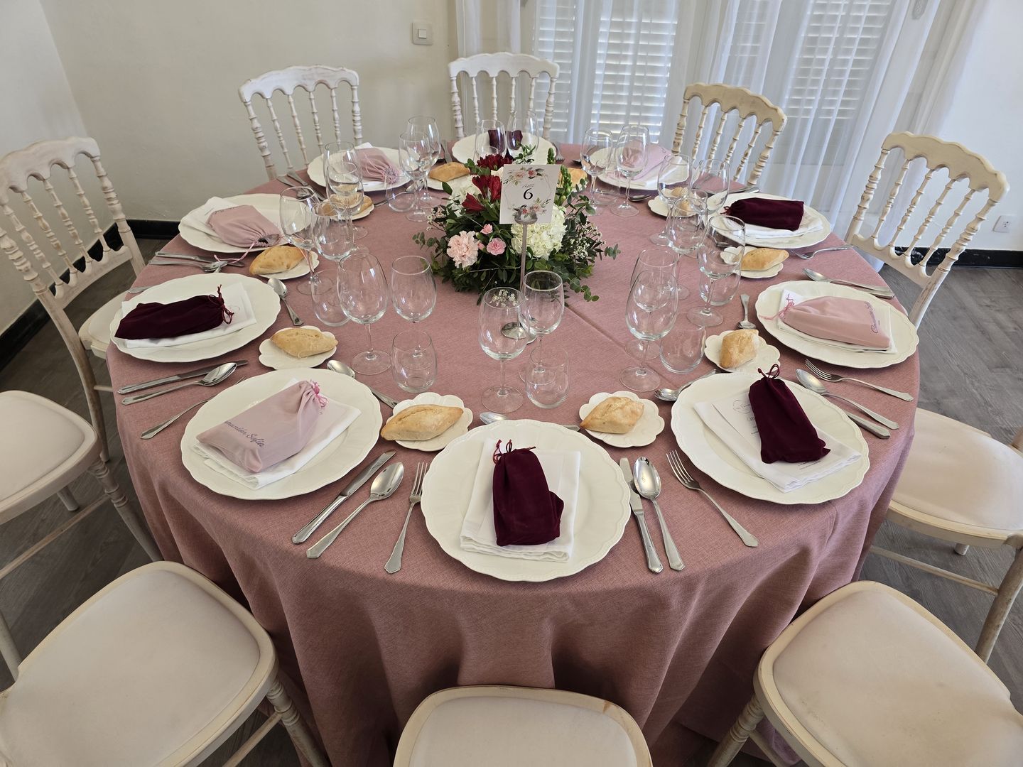 Mesa redonda vestida con mantel rosa empolvado, cristalería y centro floral
